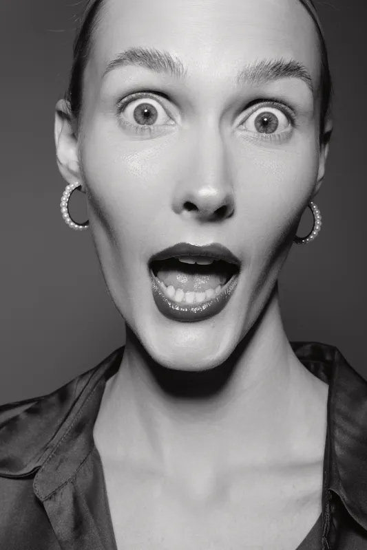 Surprised white woman with pale skin and earrings looks amazed with wide open eyes and mouth in black and white portrait studio shot.