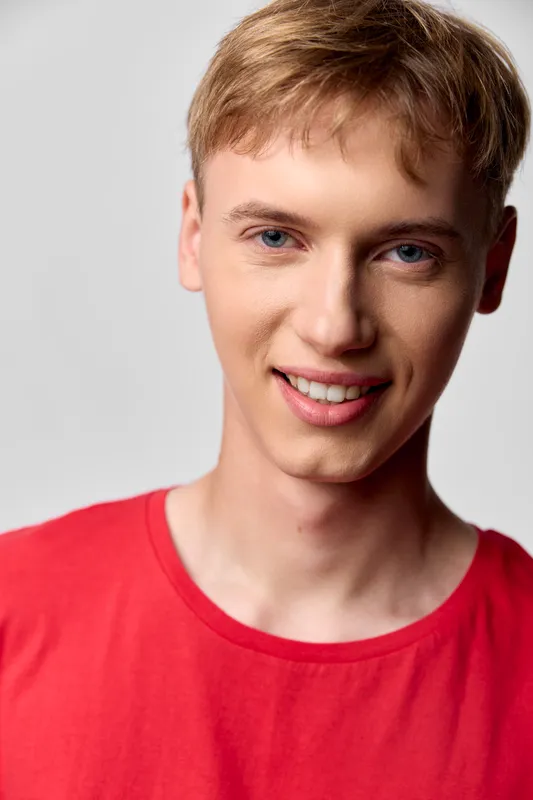 Smiling young man wearing a red shirt in a studio setting, clean background, warm light, friendly expression suitable for lifestyle, fashion, technology and corporate concepts