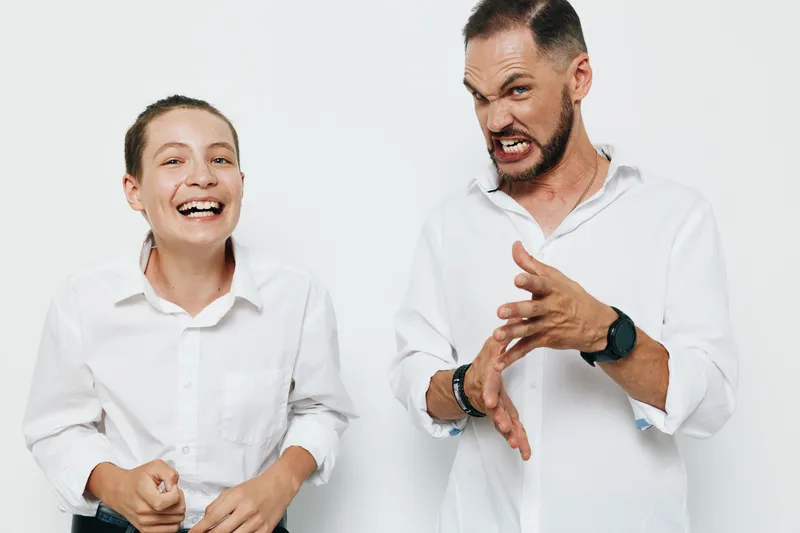 A professional business scene with a confident man and an excited colleague against a solid color background, highlighting emotions of enthusiasm and playful intensity.