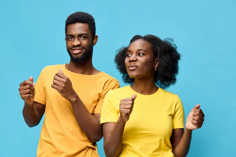 Young Black couple dancing joyfully against a bright blue background, wearing matching yellow outfits exuding happiness and connection, ideal for celebrating love and togetherness