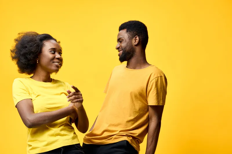 Happy young African couple sharing a joyful moment in matching yellow outfits against a bright yellow background, exuding positivity and connection