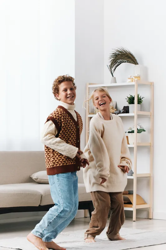Two cheerful children dance playfully in a bright living room, wearing cozy sweaters and jeans, capturing carefree energy and warm, vivid family moments.