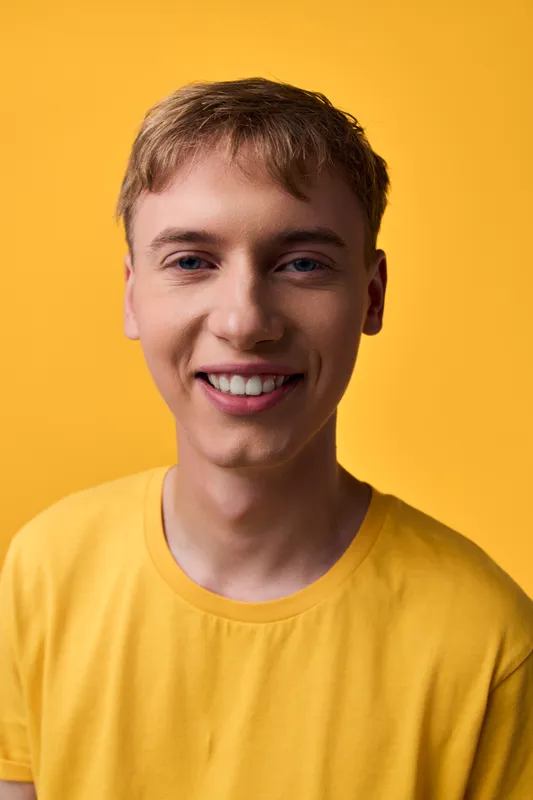 Smiling young man wearing a yellow tee against a vibrant yellow backdrop, conveying happiness, optimism, and casual style for lifestyle, fashion or wellness marketing