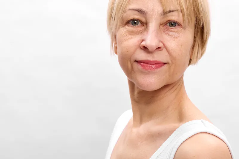 Woman applying face cream in closeup portrait, smiling mature features, studio lighting on white background, skincare routine for wellness and selfcare, gentle hydration