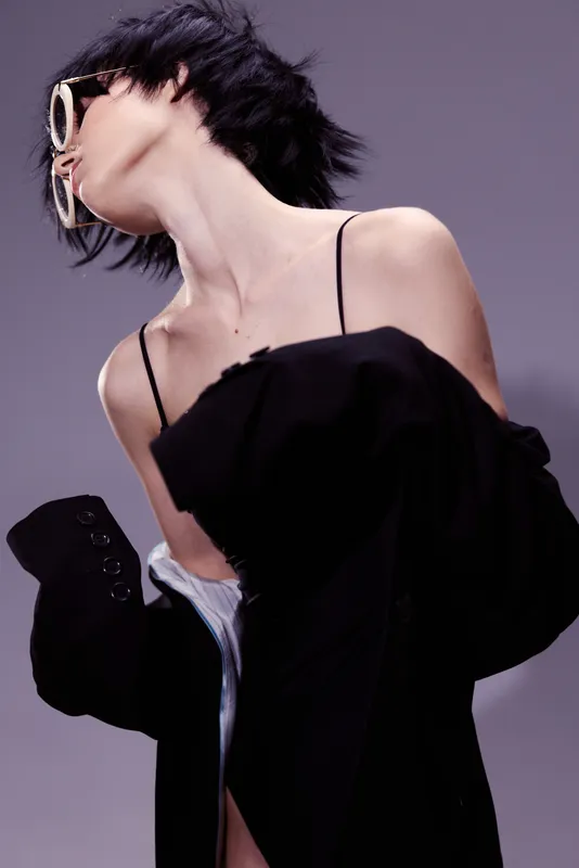 Stylish woman wearing sunglasses and black jacket with dynamic pose, short hair, and modern fashion style.