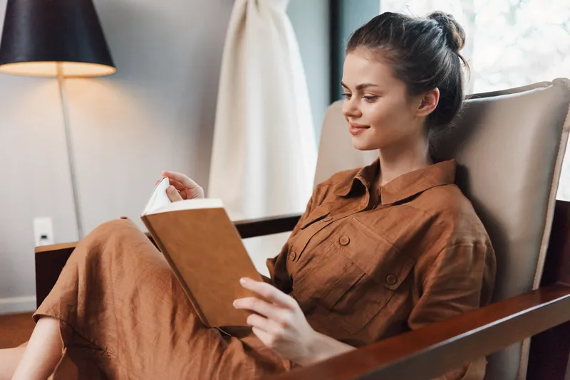 Молодая женщина в стильном коричневом наряде отдыхает, читая книгу в современном уютном пространстве