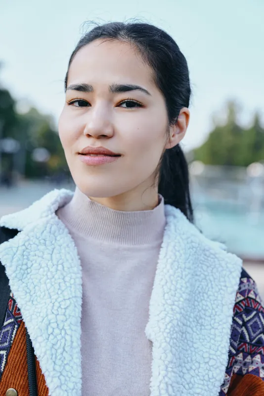 Young woman outdoors wearing a cozy fleece jacket and light sweater, calm face with soft daylight, blurred nature background, fashion lifestyle image for streetwear and casual style