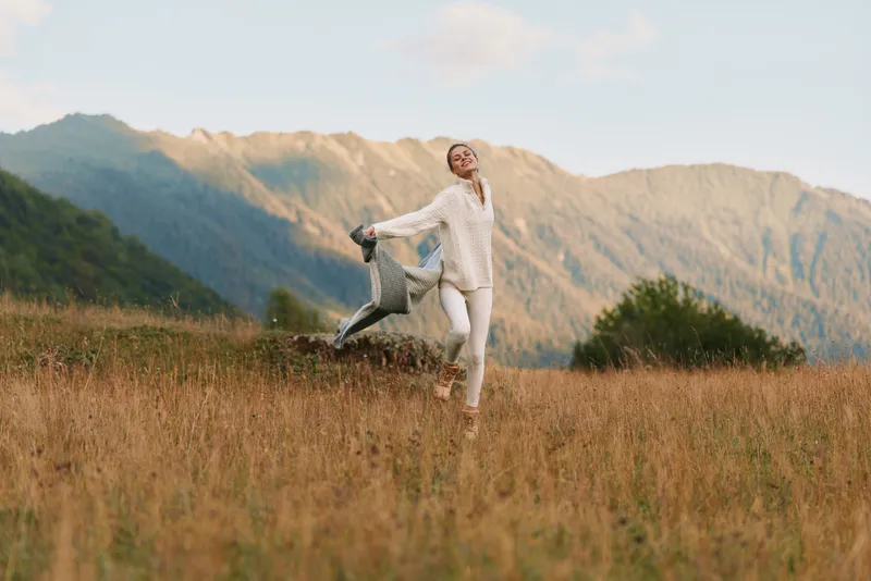 Happy woman running with child in open field, enjoying nature, casual clothes, warm sunlight, mountain background, joyful moment, lifestyle outdoors