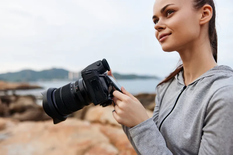 Young woman with a camera on the beach, showcasing photography passion and creativity in a serene coastal landscape