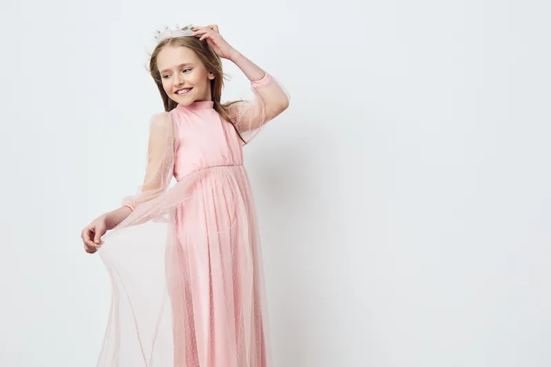 Young girl wearing a pink dress, radiating joy and confidence, with a playful expression against a soft white background, perfect for children s fashion concepts
