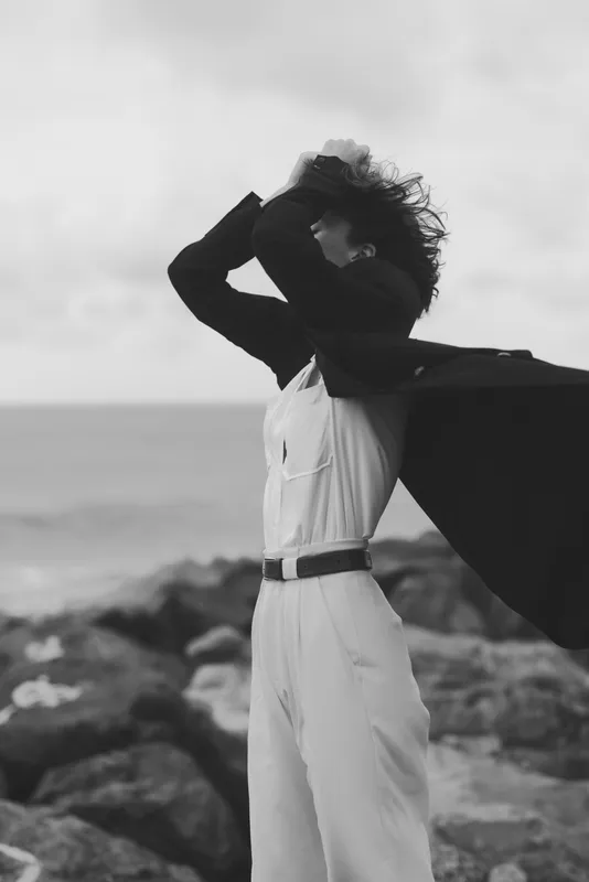 Cape, wind, coast, silhouette, dramatic, suit, woman, fashion, ocean, breeze, windblown, monochrome, drama, motion, freedom on a windswept rocky shore with a bold stance