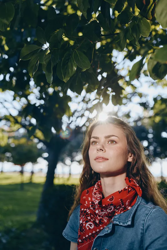 lifestyle woman in modern boho-western denim street style with red bandana and natural sunlight, captured in warm film color for artistic outdoor vibe