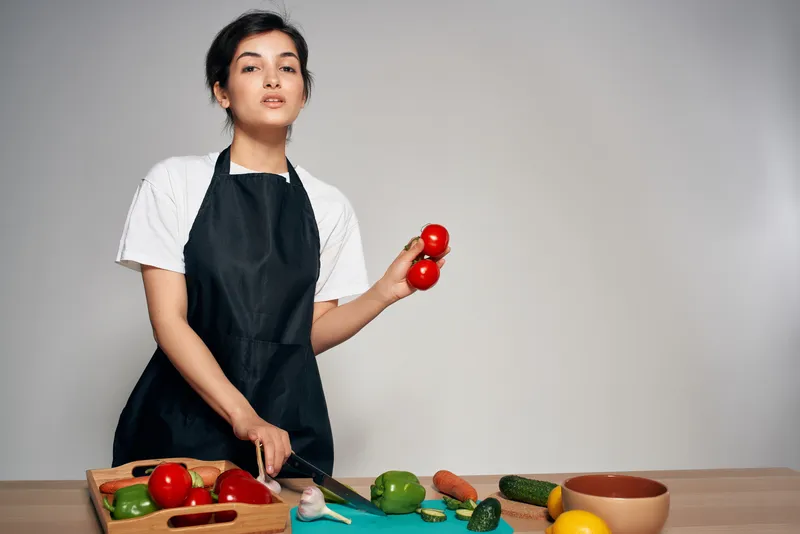 Женщина в черных фартуках на кухне с овощами для здоровой пищи