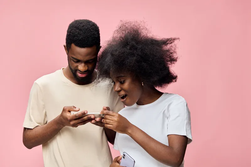 Happy couple discovering something exciting on their smartphones against a pink backdrop, capturing the essence of modern relationships and technology
