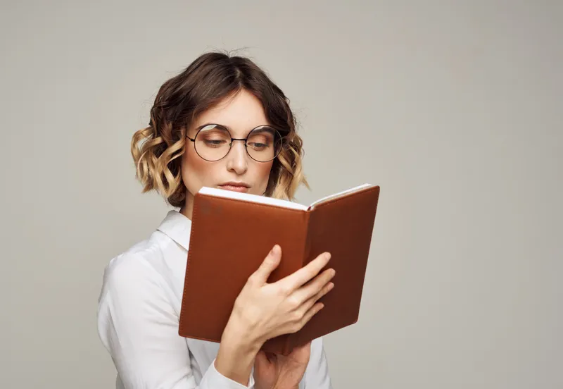 Женщина в очках держит в руке книгу на сером фоне