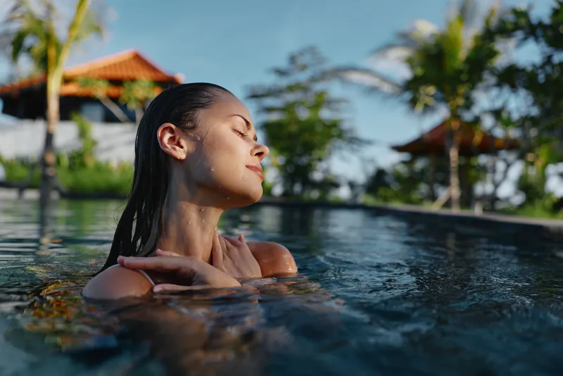 A poolside woman rests in calm, sunlit water, savoring relaxation and serenity in a tropical vacation scene, with palm shadows and a gentle breeze framing a quiet, blissful moment