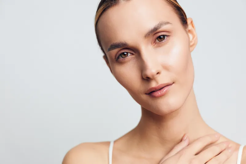 A close-up portrait of a calm woman with a neutral expression, soft lighting, and clear skin in a minimal studio setting. Concept for natural beauty, self-care, and wellness.