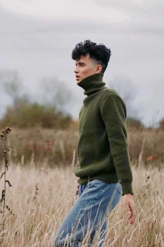 A young man walks through tall field grass in a green turtleneck and jeans, a candid portrait capturing natural posture and intimate emotion, highlighting authenticity and subtle documentary