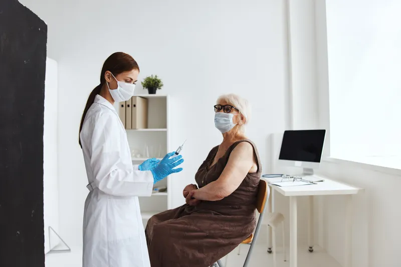 Пациент получает инъекцию шприцем для вакцинации, рядом лежит паспорт вакцинации, на фоне больничное лечение