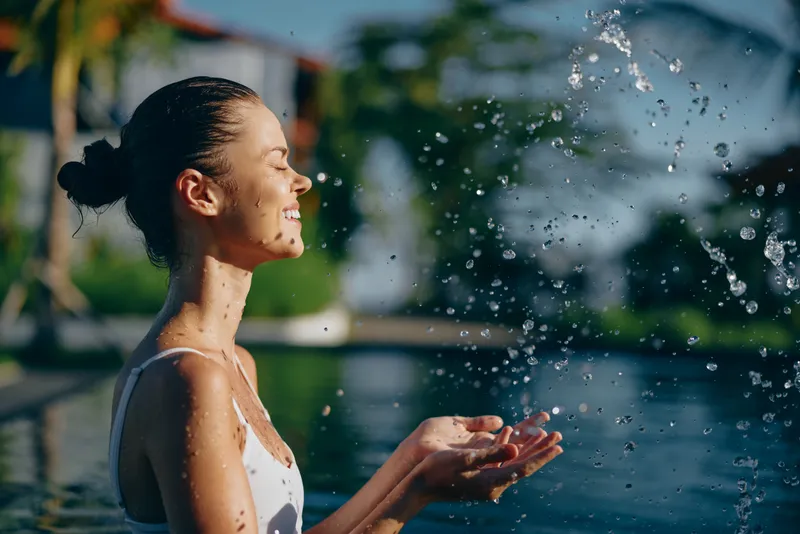 Portrait of a woman, smile and water splash by pool, in outdoor leisure scene capturing summer happiness.