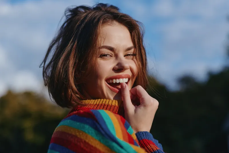 Woman, smile, striped sweater, outdoor, portrait, playful young adult model in her mid 20s laughing and biting finger, casual colorful knit, short brown hair, candid lifestyle fashion image.