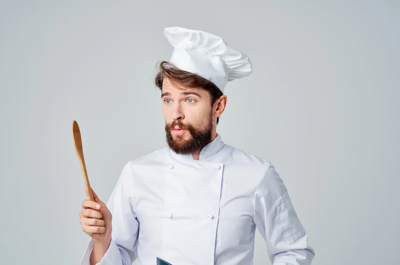 Весёлый шеф-повар мужского пола на кухне ресторана с кухонной утварью