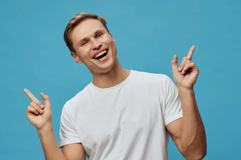 smiling happy young caucasian man in white t-shirt pointing up isolated on blue background digital detox positivity concept