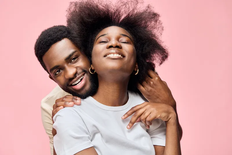 African couple enjoying each other s company, smiling against a pastel pink background, showcasing love and happiness in a modern lifestyle setting