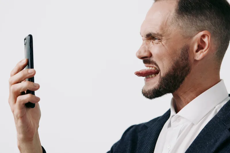 Professional man in a suit with a bright colored background, expressing playful emotion while looking at a smartphone, ready for business communication and creative dialogue.