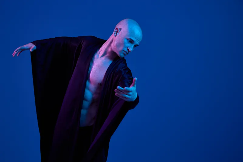Captivating man in a flowing robe, striking a dynamic pose. The image features light blue tones, adding depth and emotion to the black and white scene.