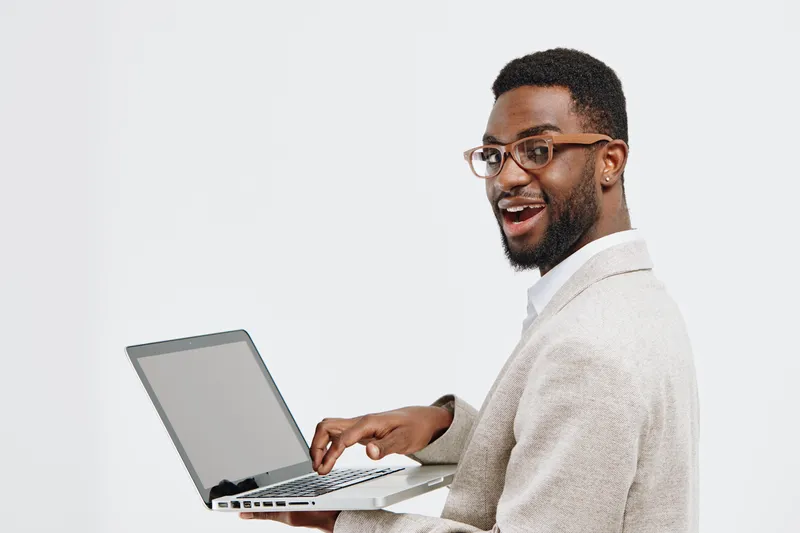 Smiling man with glasses working on laptop in casual sweater isolated on plain white background, creating a friendly, professional atmosphere. Modern and cheerful image suitable for technology, work, 