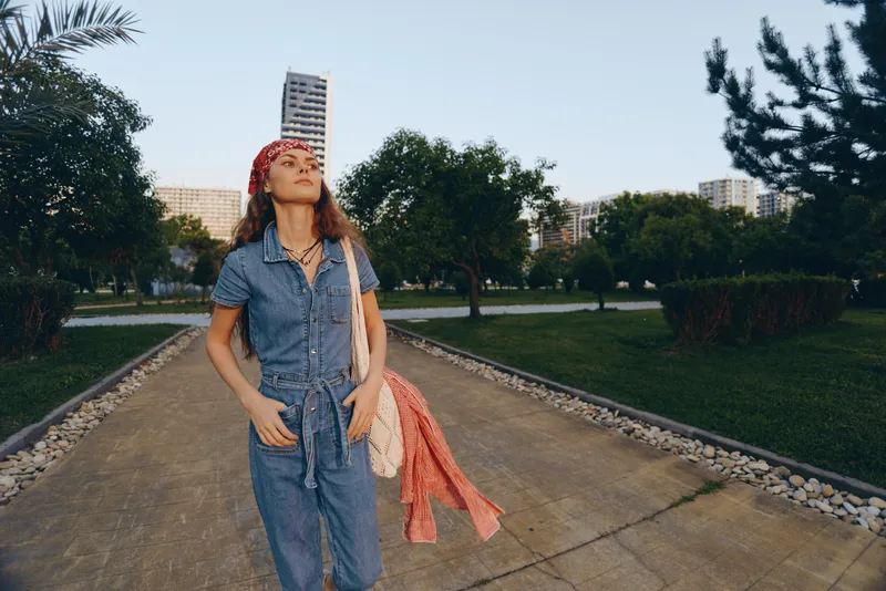 Lifestyle woman in modern boho-western denim street style walking outdoors with red headscarf, relaxed mood, urban park background, film color tones.