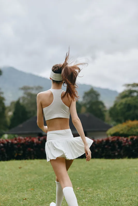 Young athletic female model in white sportswear enjoys nature, showcasing a healthy lifestyle and emotional freedom while running outdoors in summer