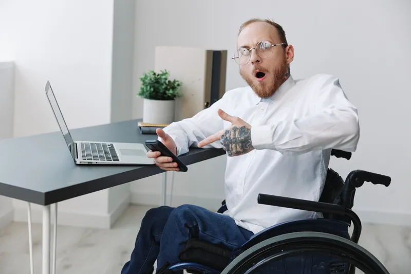Мужчина в инвалидной коляске работает в офисе за ноутбуком, работа онлайн, социальные сети и стартап, свободное место для копирайтинга, интеграция в общество