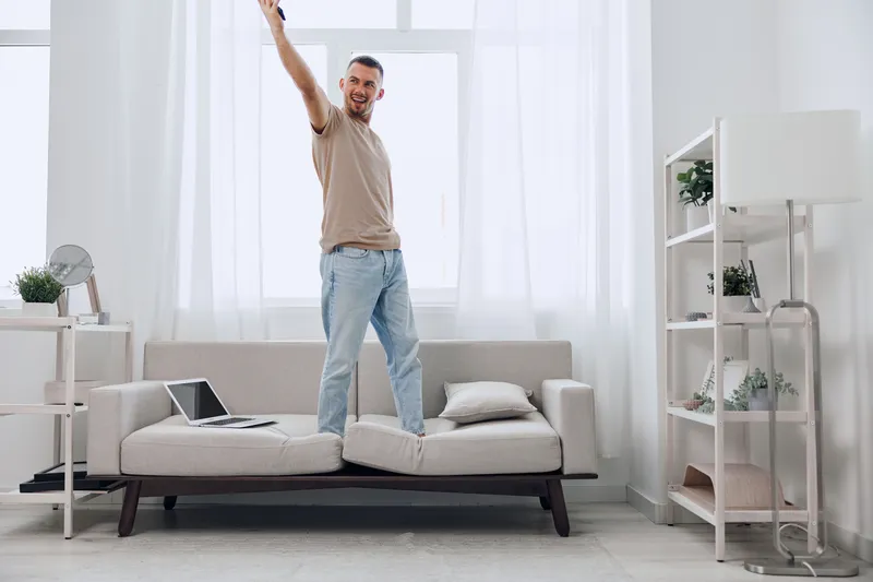 Energetic man celebrating on a couch, surrounded by a bright, modern interior. This scene captures the essence of optimism and joy in a contemporary living space.