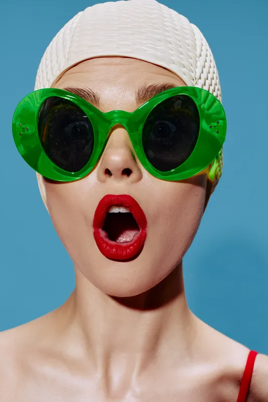 Крупный портрет удивлённого пловца в шапочке для плавания на голубом фоне