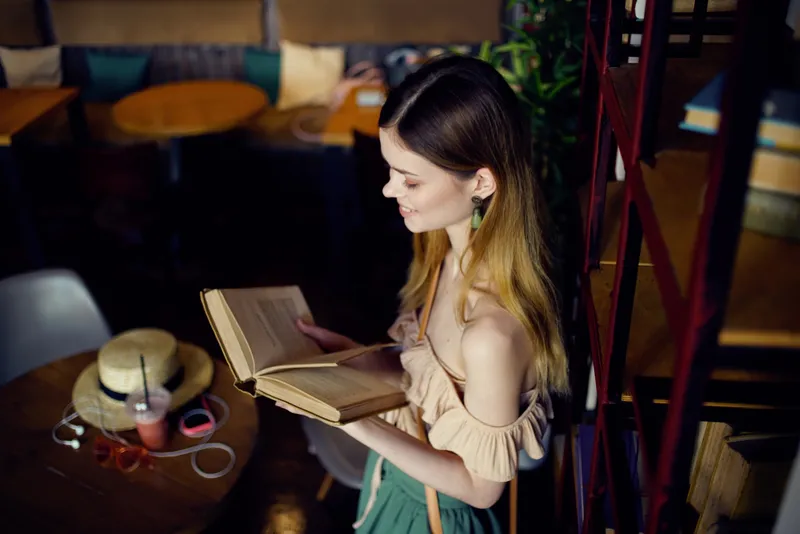 Симпатичная женщина в кафе с книгами, отдыхает в интерьере ресторана, ведет определенный образ жизни