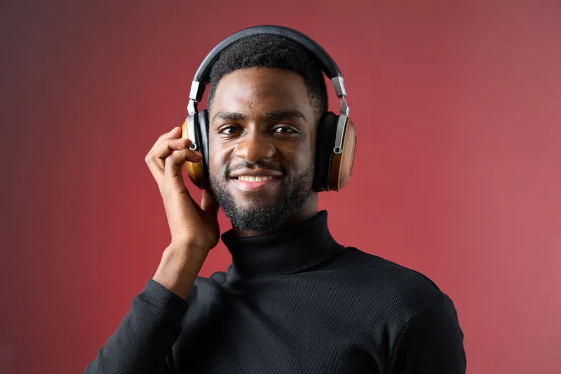 Smiling young African man wearing headphones against a vibrant red background, showcasing joy and engagement with music, perfect for tech and lifestyle themes