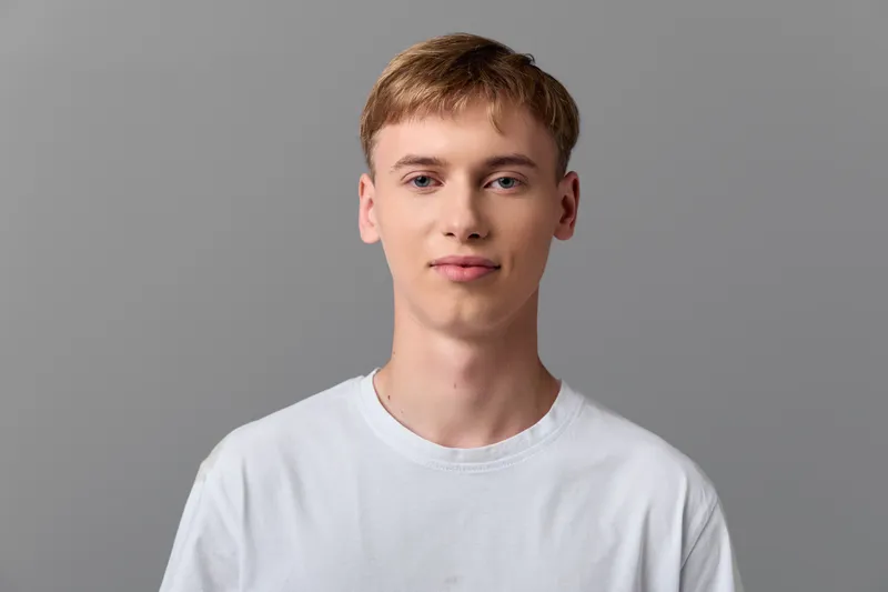 Man in white t shirt looking at camera, simple studio setup with neutral gray background, clean minimal look, thoughtful expression, suitable for stock photography, versatile and approachable.