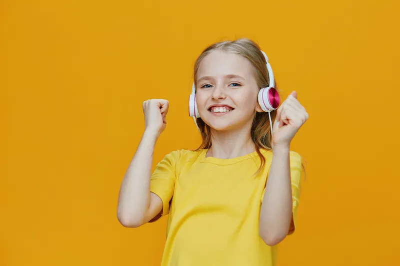 Happy girl in yellow t shirt dancing with headphones against vibrant yellow background, expressing joy and excitement, perfect for kids music or lifestyle themes