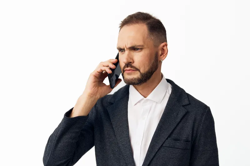 Portrait of a business professional man on a clean isolated colored background. He speaks on the phone, projecting focus, confidence, and calm determination in business.