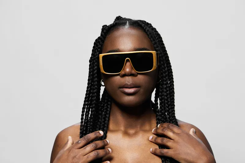 Confident woman with braided hair wearing stylish sunglasses against a neutral background, exuding modern elegance and empowerment