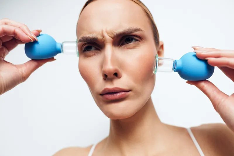 Woman facial massage skincare spa beauty hands blue massage tools on her cheeks, calm female portrait on white background, skincare therapy for hydration and rejuvenation, closeup beauty care