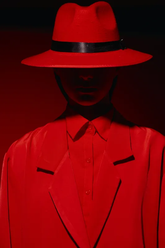 Mysterious fashion model in red avantgarde outfit, hat shadowing face, studio shot with dramatic lighting. Concept for beauty, creative editorial, style, and fashion art.