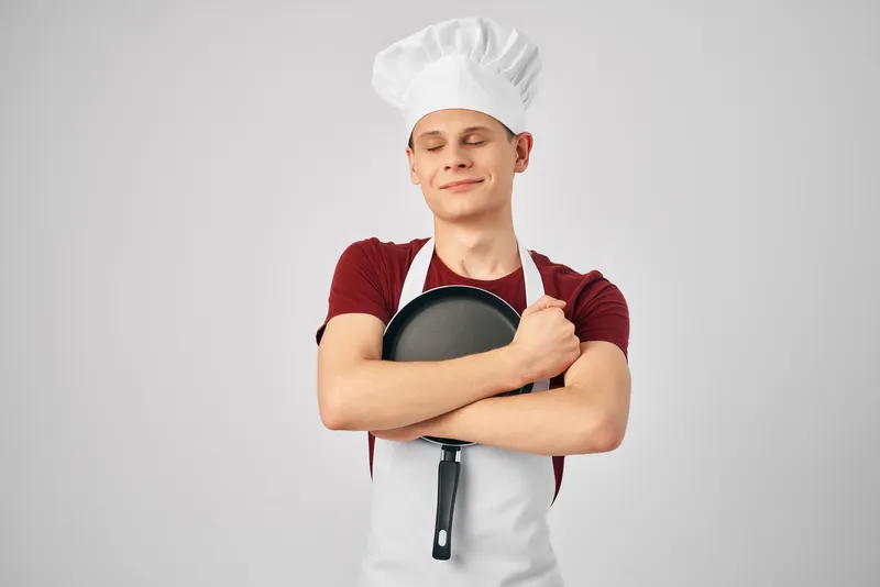 Повар в униформе держит сковороду в руках на профессиональной кухне ресторана