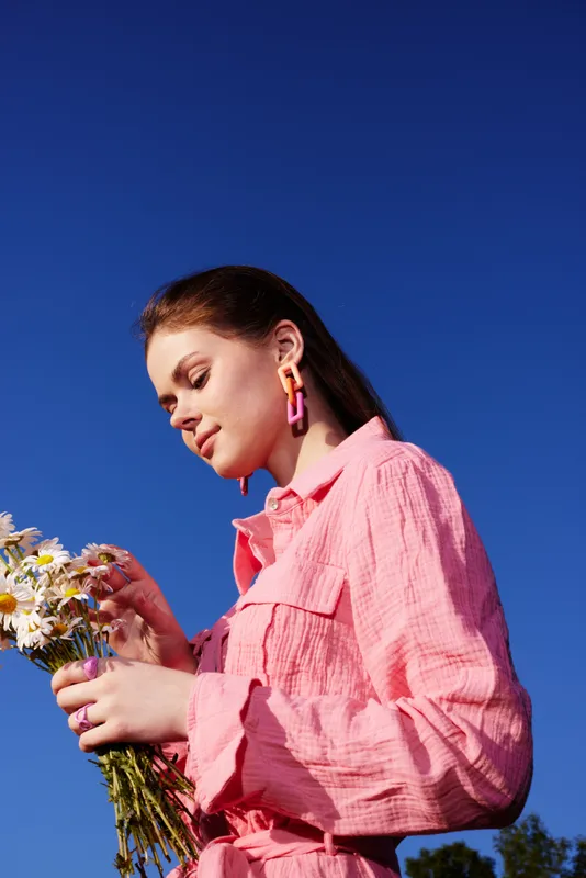 Young woman in a pink outfit holding flowers against a clear blue sky, exuding joy and connection with nature, perfect for spring themed projects