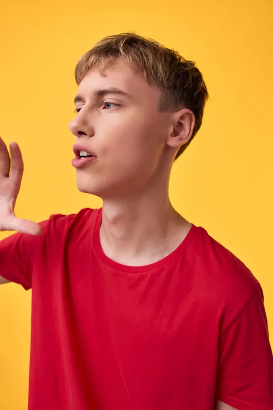 Man in a red t shirt makes a bold hand gesture against a bright yellow background, capturing energy, clarity, and expressive communication in a studio scene suitable for advertising and lifestyle