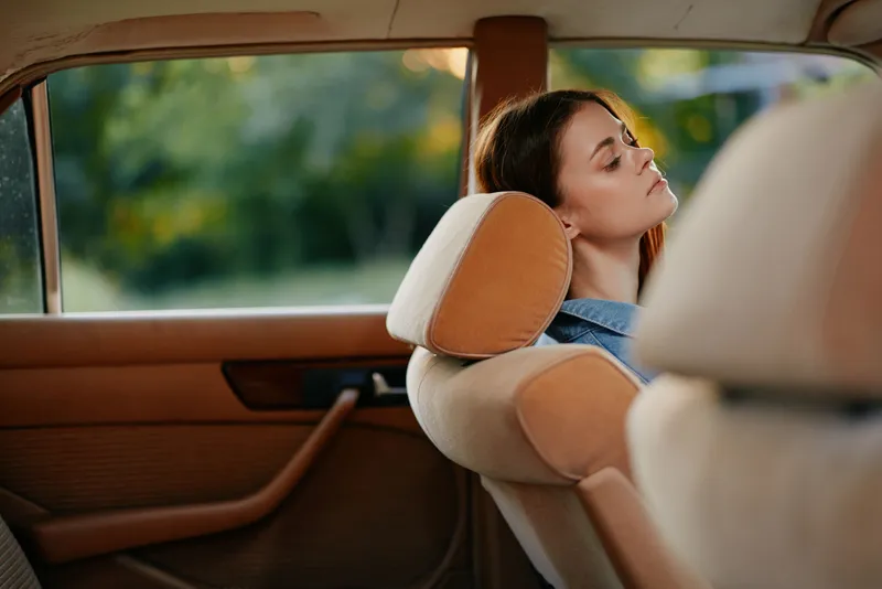 Relaxed young woman enjoying peaceful moments in a vintage car during a sunny day, capturing serenity and nostalgia with soft colors and nature in the background.