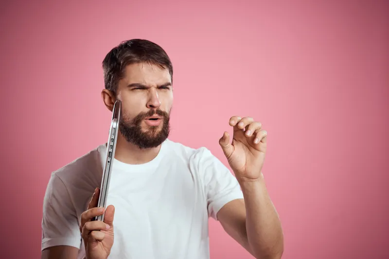 Эмоциональный мужчина с закрытым ноутбуком в руках на розовом фоне, обрезанный вид, свободное пространство