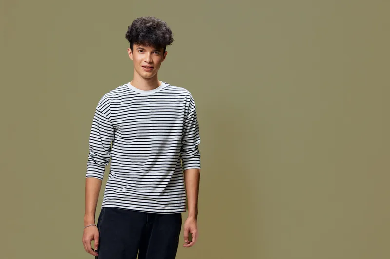 young man wearing a striped shirt standing against a plain olive background, casual style with confident expression and relaxed posture in studio lighting